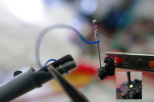 Nachbildung des Experiments von H. J. Rounds: Eine negativ geladene Nadelspitze auf Siliciumcarbid erzeugt einen grün glimmenden Schottky-Kontakt.